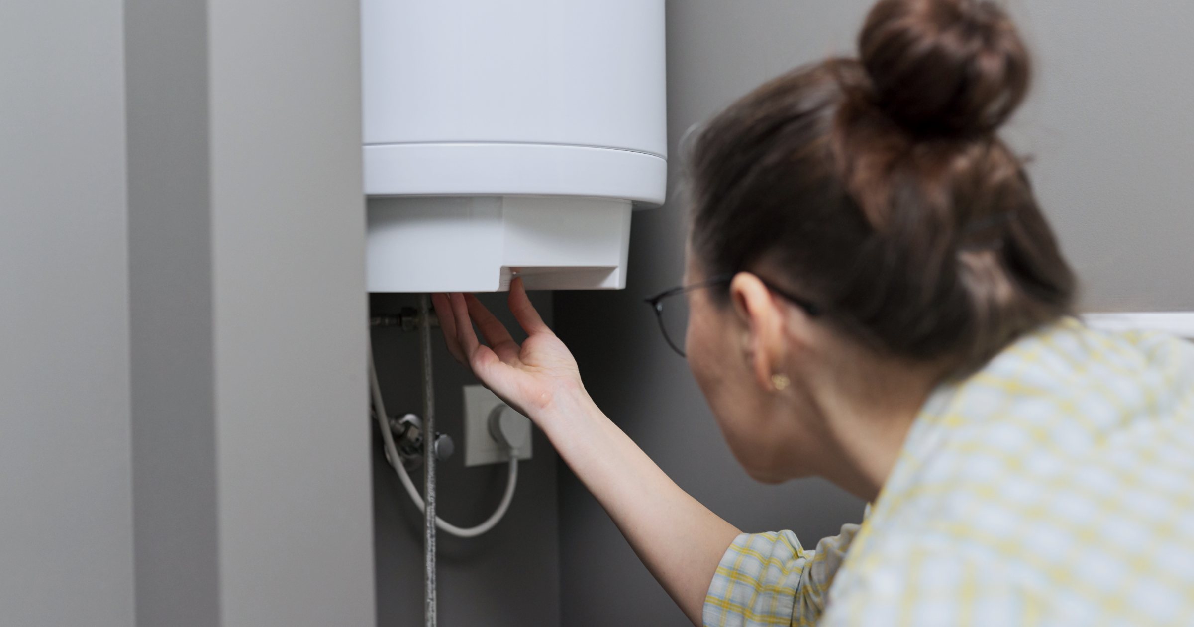 Boiler electric de apă caldă montat pe perete, cu o persoană care reglează comenzile din partea de jos a rezervorului