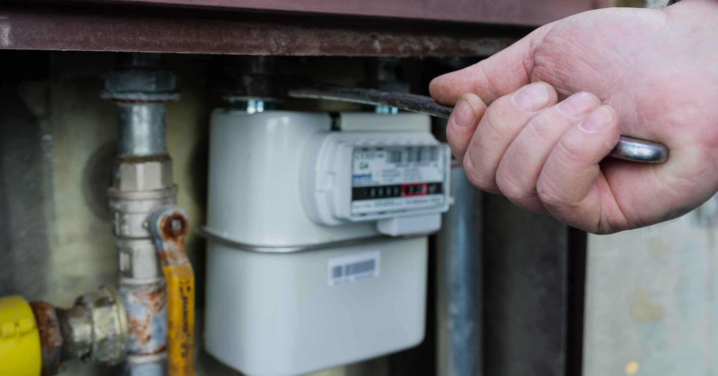 Mâna unui instalator care reglează contorul de gaz al unei locuințe, lângă țevile de cupru și conducta galbenă de gaz a branșamentului