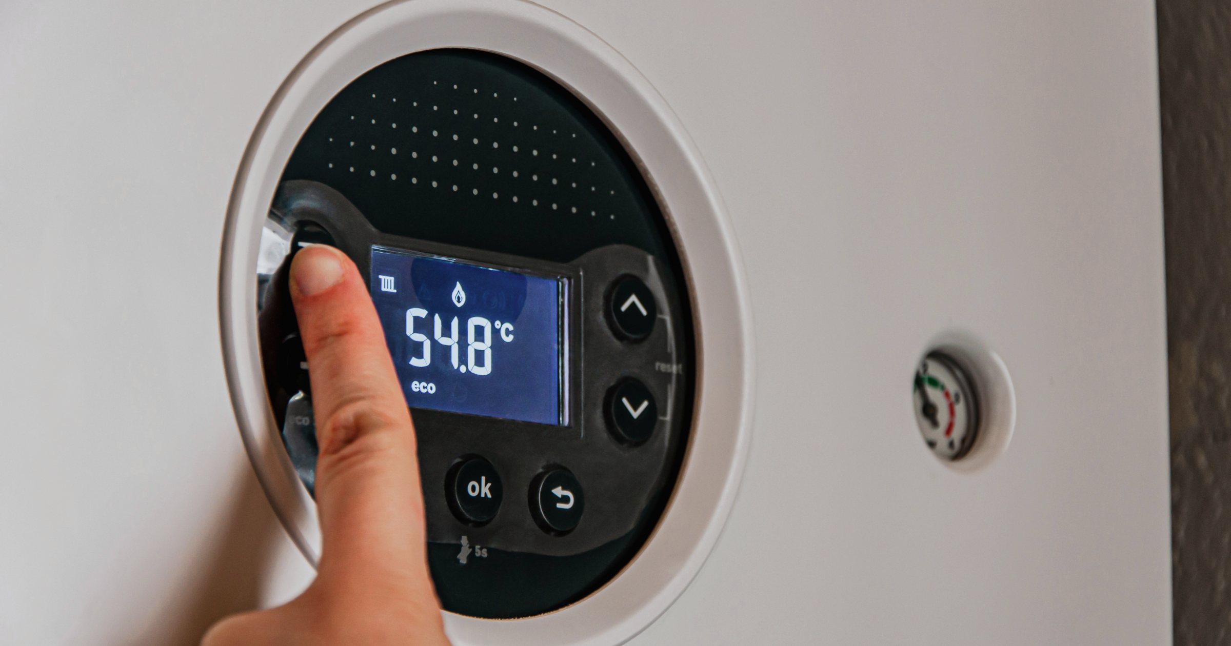 Mână care reglează panoul digital al unei centrale termice pe gaz montată pe perete, cu afișaj care indică temperatura