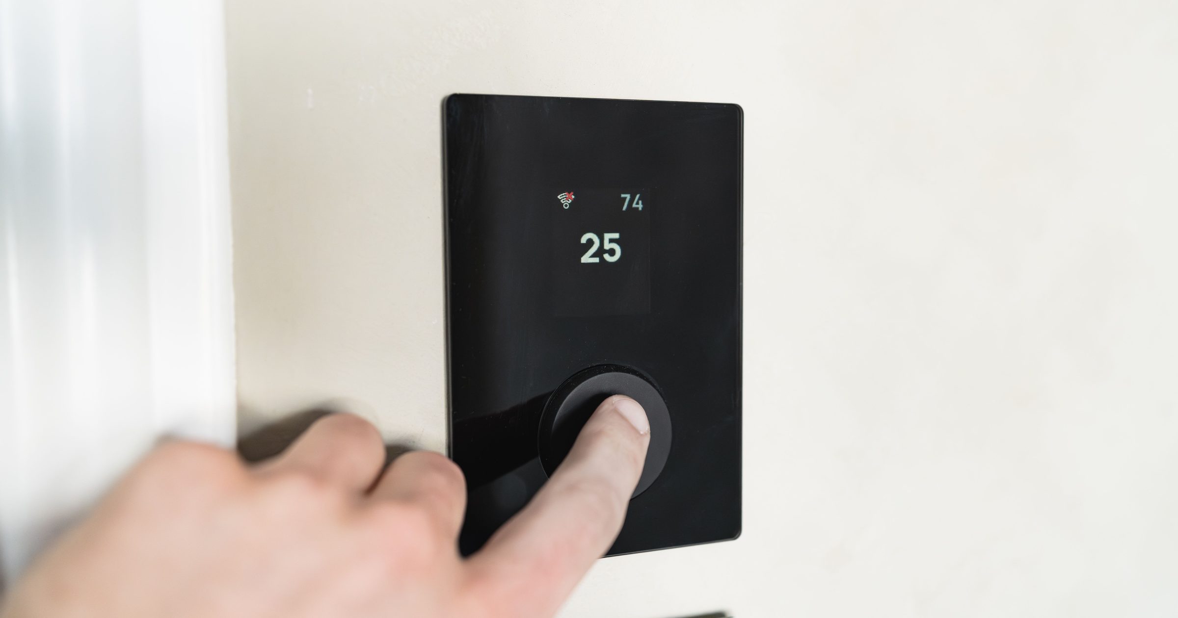 Deget apăsând pe un termostat de perete care afișează temperatura setată