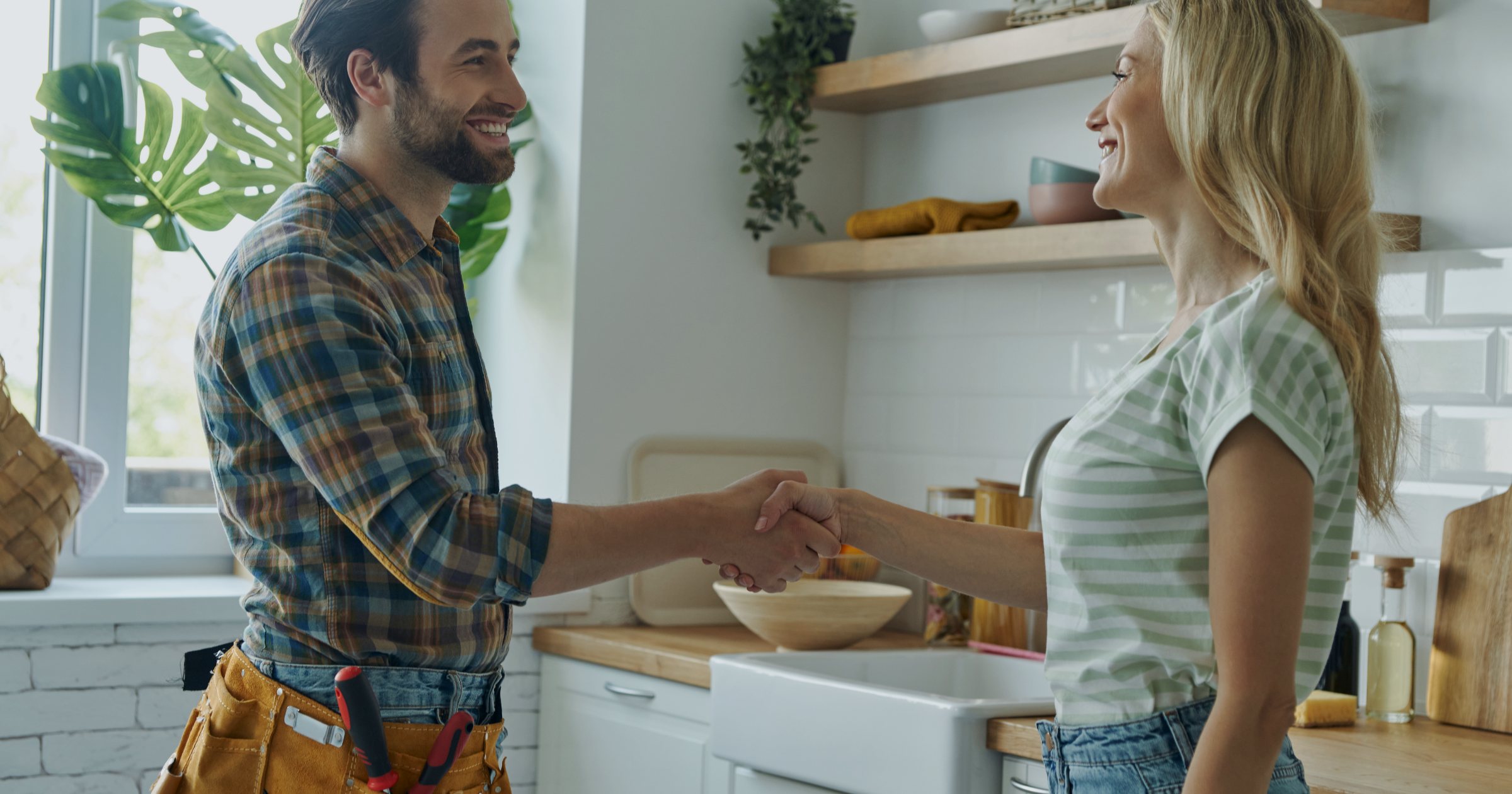 Instalator cu centură de scule strânge mâna unei cliente în bucătărie, după finalizarea unei lucrări