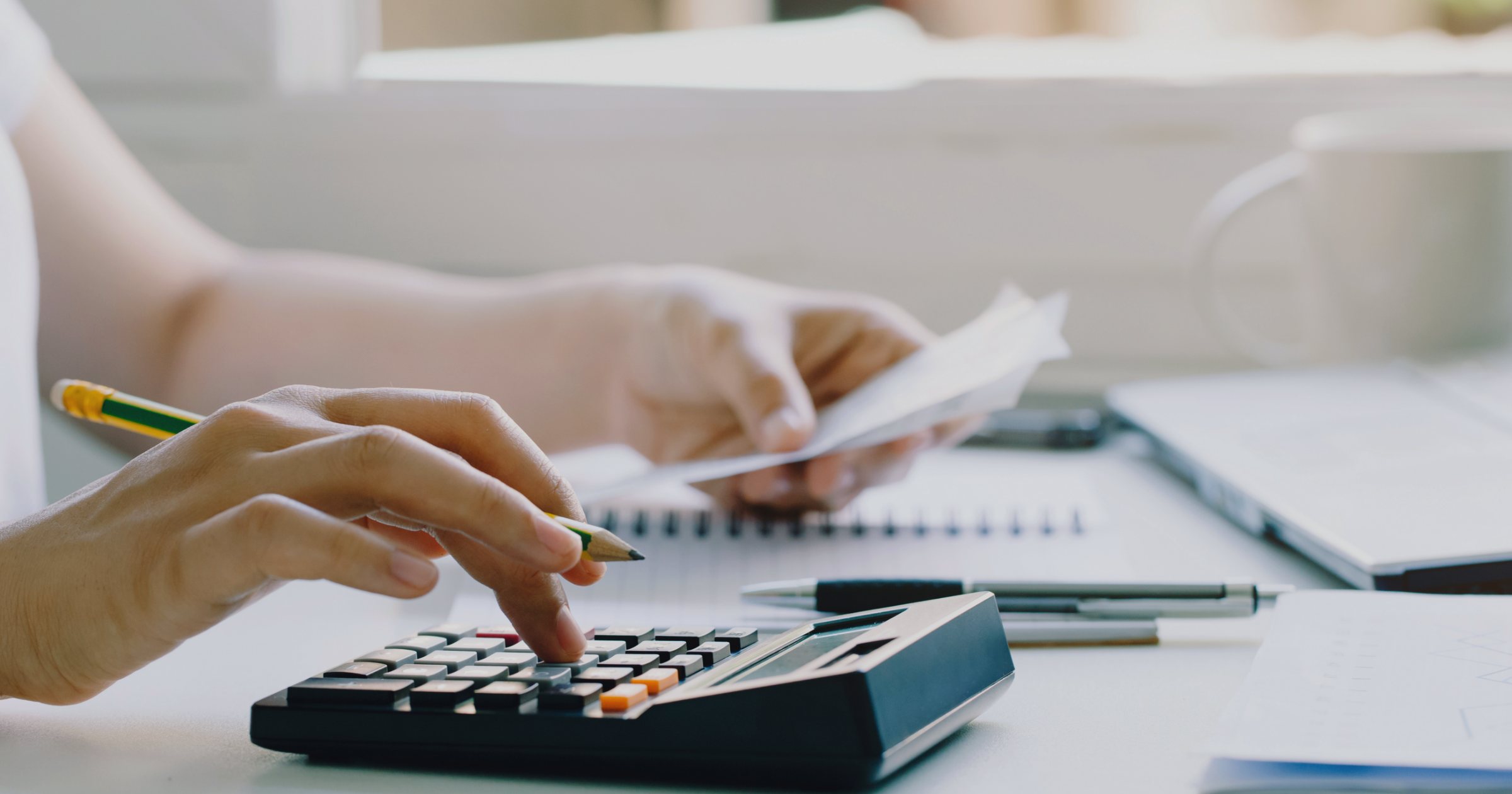 Persoană care verifică o factură ținând chitanța într-o mână și folosind un calculator pe birou